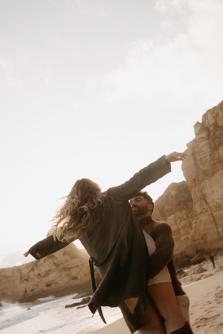 Un couple sur la plage dans la région de l'Algarve au Portugal. L'homme porte sa femme dans les bras pendant qu'elle fait l'avion.