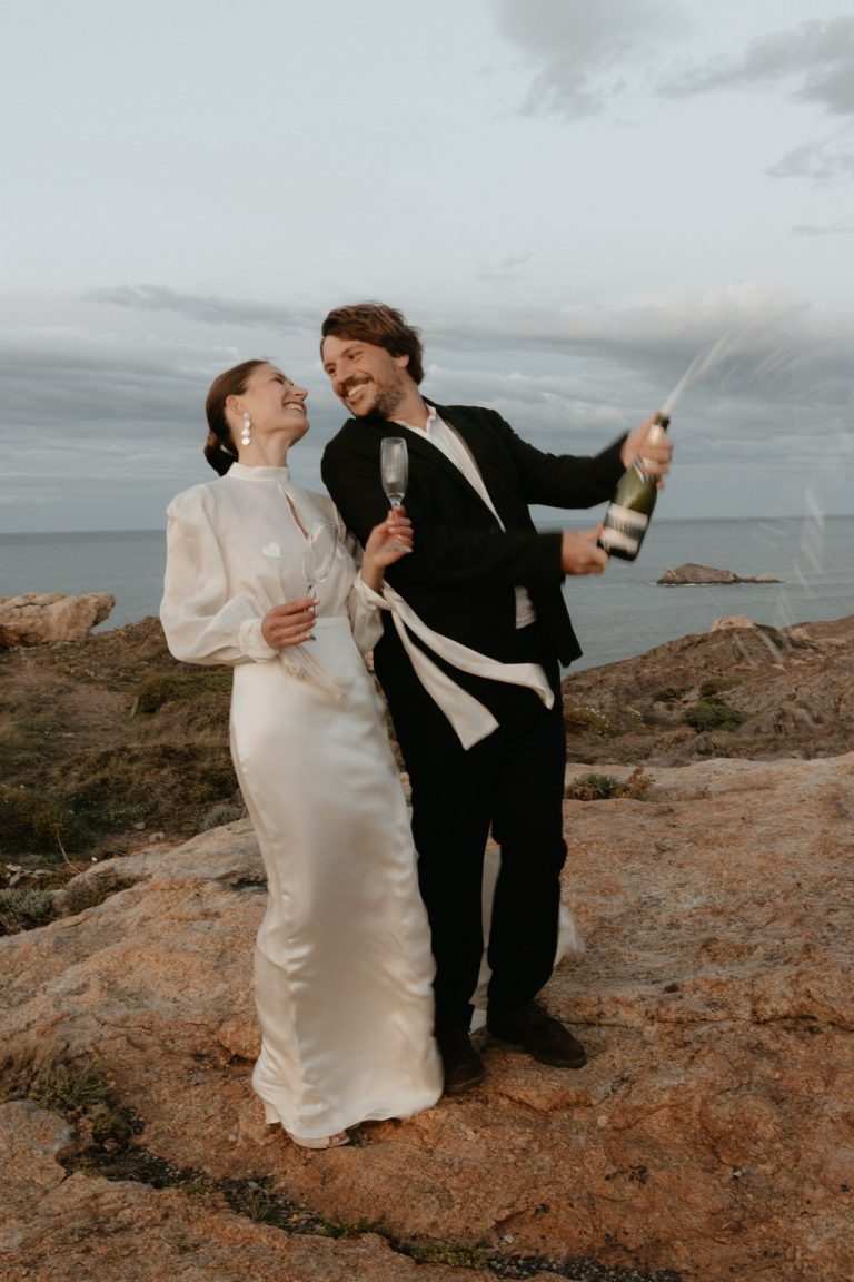 Un couple célèbre leur mariage avec une bouteille de champagne. Ils se regardent en riant. Un moment fun capturé par par Lesley Sanchez, photographe Landes.