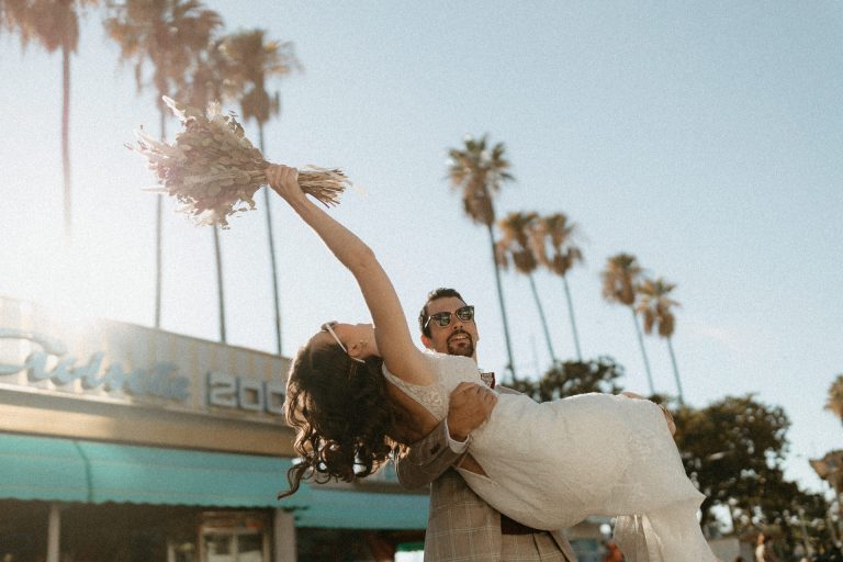 Le marié porte sa femme après leur cérémonie de mariage. La mariée brandit son bouquet vers le ciel pour célébrer leur bonheur.