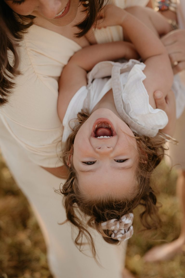 La maman joue avec sa fille. L'enfant éclate de rires. Elles passent un bon moment ensemble pendant leur séance photo avec par Lesley Sanchez, photographe Landes.
